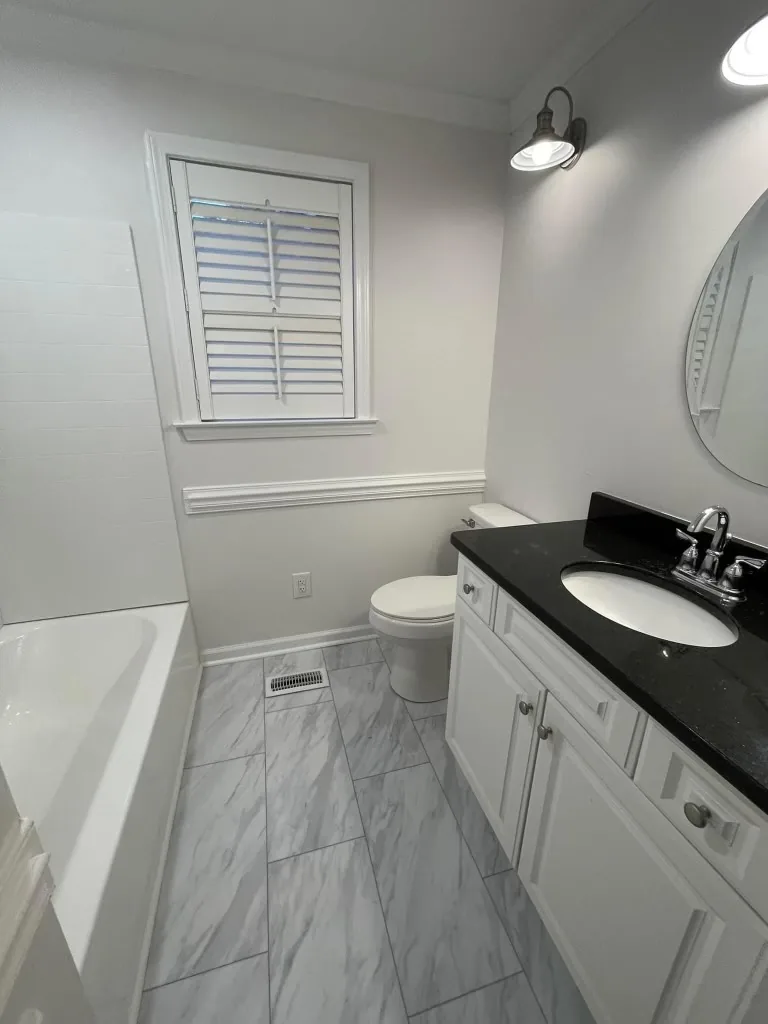 A bathroom with a marble-surround tub, vanity and plantation shutters