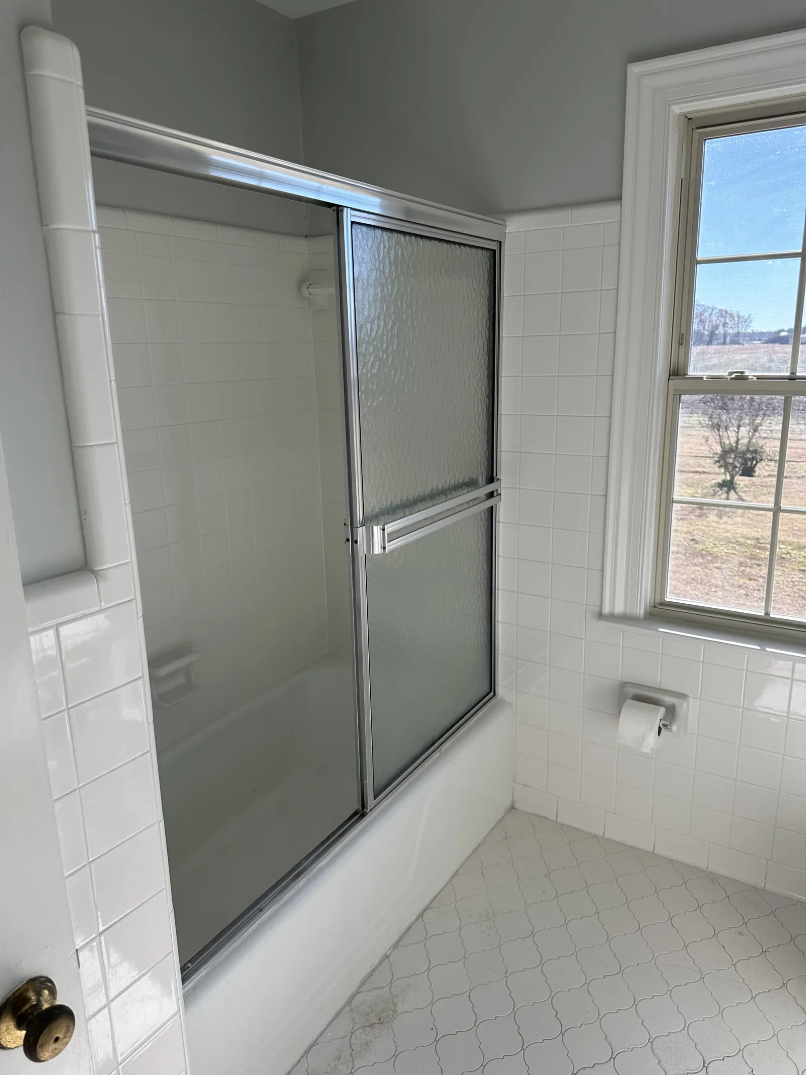 A bathroom with a sliding glass shower enclosure beside a window