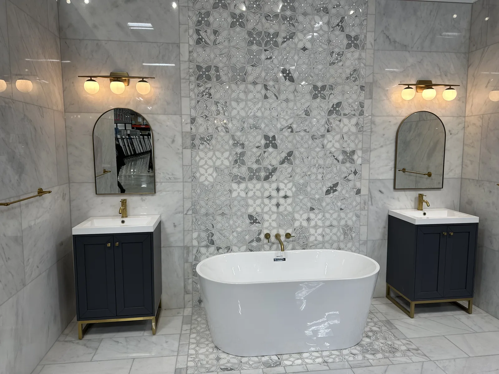 A freestanding tub between twin navy vanities against a patterned marble wall