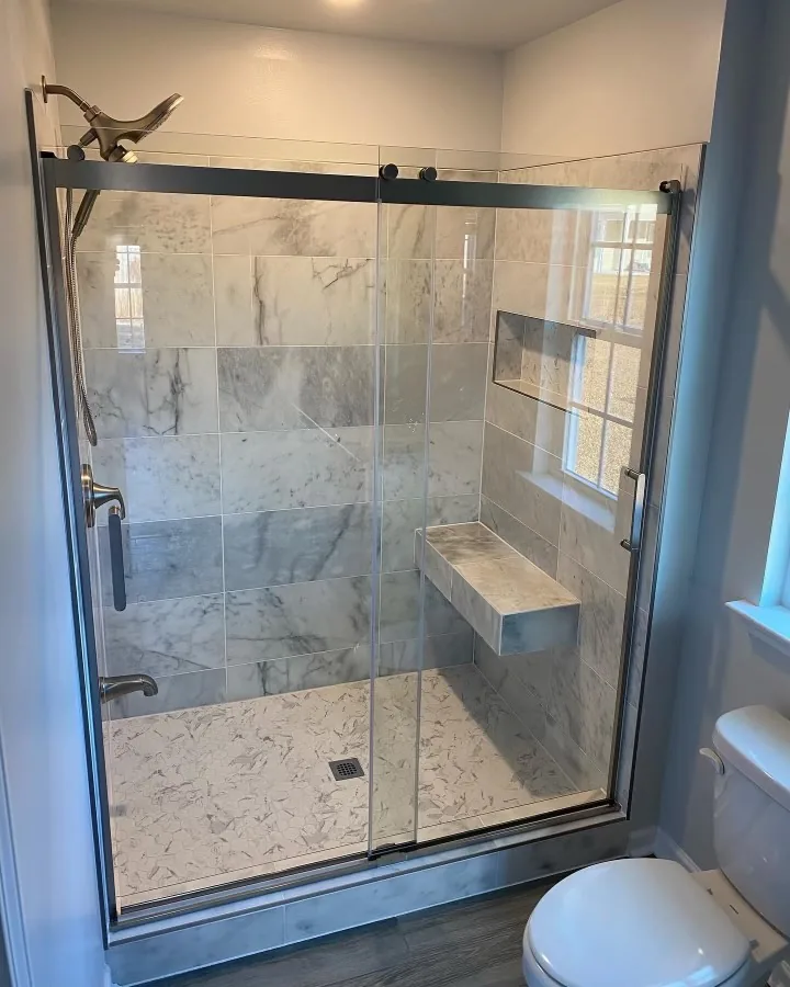 A walk-in shower with grey marble-effect tile and a sliding glass door
