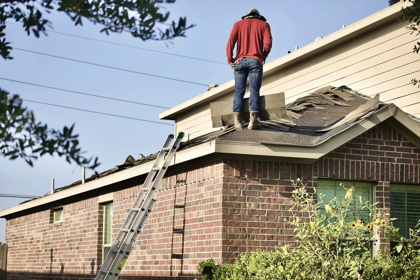A residential roof part-way through a tear-off, with a ladder up to the eaves